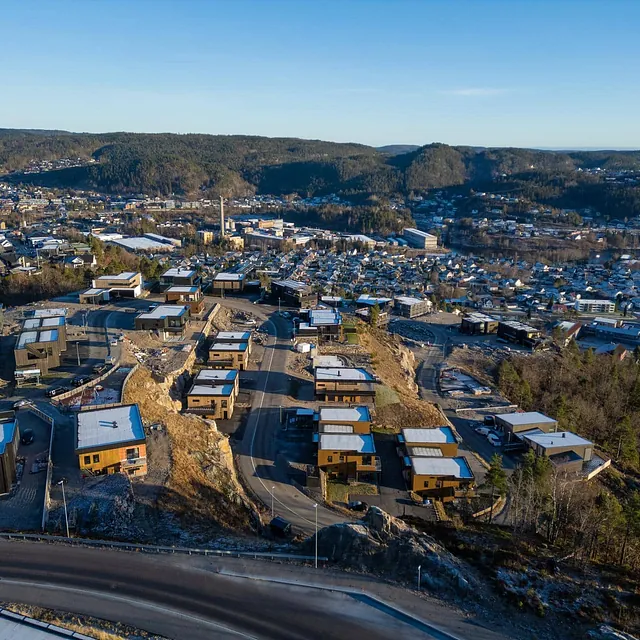 Dronebilde av nytt boligfelt i åsside med utsikt over by og skog.